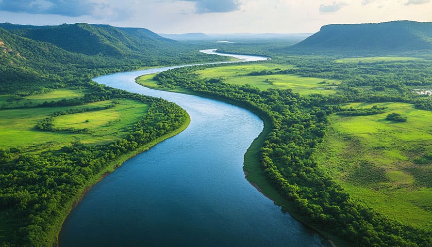 A winding river flows through green fields and hills under a partly cloudy sky.