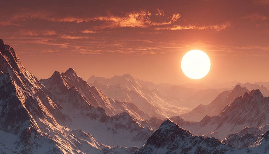 Sunset over snow-covered mountain peaks with cloudy sky in the background.