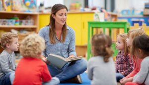 A woman reads a book to a group of young children sitting in a circle in a classroom.
